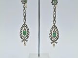 une paire de boucles d'oreilles en argent et émeraude, présentée sur un présentoir