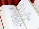an open book sitting on top of a table next to a stack of red books