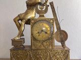 a gold clock with a woman playing a musical instrument on it