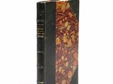an old book with a black cover sitting on top of a white surface