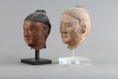 paire de sculptures représentant des têtes asiatiques posées sur un socle en acrylique, sur fond gris