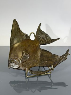 brass fish sculpture on stand on grey surface with white background