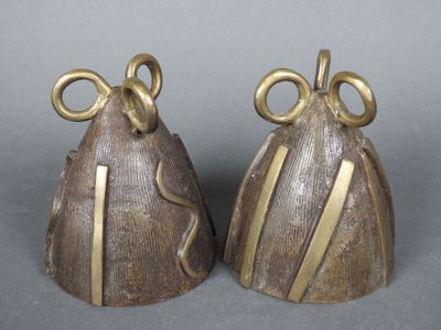 une paire de clochettes en laiton ornées de nœuds, posées sur une surface grise
