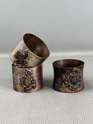 three antique silver napkins and a silver cup on a white surface
