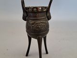 un petit vase en bronze posé sur un socle, sur une surface blanche