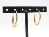 un gros plan sur une paire de boucles d'oreilles créoles en or posées sur un support noir