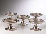 six plats plaqués argent posés sur des socles, disposés sur un fond blanc