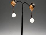 a pair of gold and white earrings on a black stand