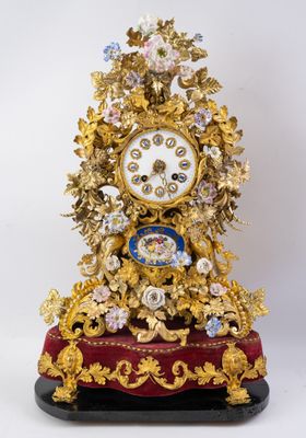une horloge dorée posée sur un socle rouge orné de fleurs