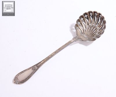 une cuillère en argent dont le manche a la forme d'un coquillage, posée sur une surface blanche