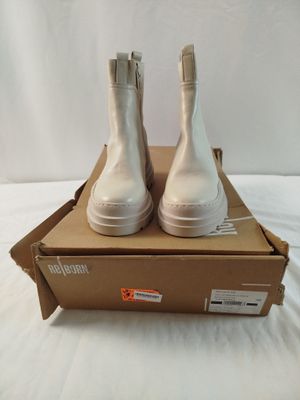 des bottes blanches dans une boîte posée sur un lit, sur fond blanc