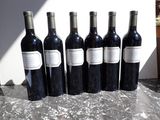 six bottles of red wine are lined up on a table