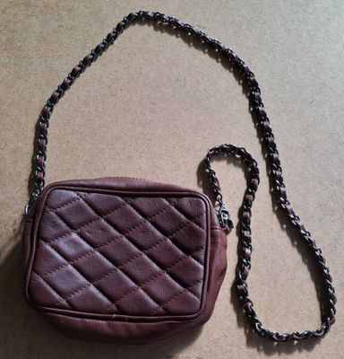 sac à main en cuir bordeaux avec bandoulière en chaîne, sur fond beige clair