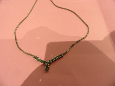 necklace with green beads on a pink surface with a shadow on the ground