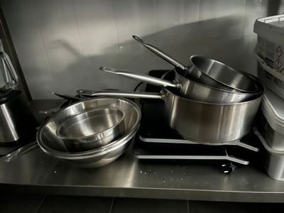 des casseroles et des poêles sont posées sur un plan de travail en acier inoxydable dans une cuisine