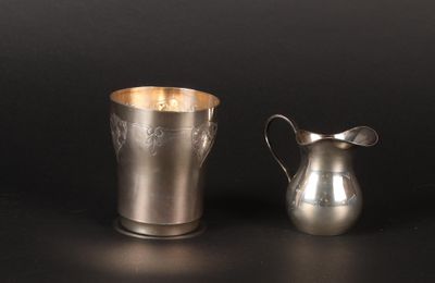 a silver pitcher next to a silver cup on a table