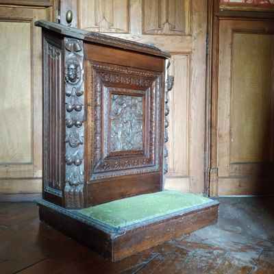une armoire en bois posée à même le sol, avec un coussin vert dessus