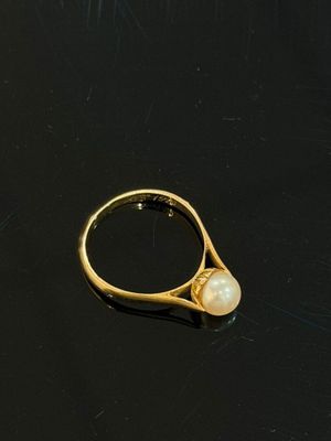 bague en or avec une perle au centre, sur un fond noir