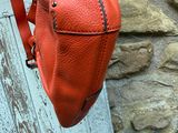 un sac à main orange accroché à une porte, avec un mur de briques en arrière-plan