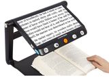 une personne en train de lire un livre sur lequel est posée une lampe loupe