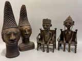 trois statues en bronze représentant des personnes assises sur des chaises, coiffées de cônes