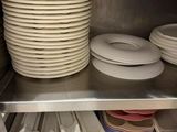 Plusieurs assiettes et bols sont empilés sur une étagère en métal dans une cuisine.