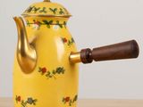 a yellow tea pot with a wooden handle on a table