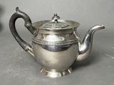 a silver tea pot sitting on a table next to a vase