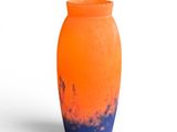 un vase orange et bleu posé sur une surface blanche
