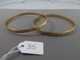 two gold bracelets on a bed with a price tag