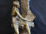 bronze statue of a woman sitting on a chair holding a book