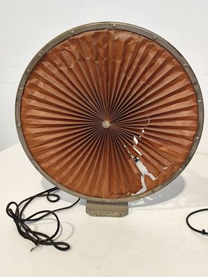 un grand ventilateur marron posé sur une table blanche, muni d'un cordon noir