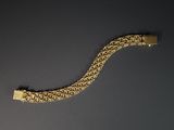 une image représentant un bracelet en or posé sur une surface noire