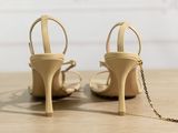 pair of nude colored high heeled shoes with a chain around the ankle