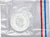 La pièce se trouve dans un sachet en plastique transparent orné d'une bande rouge, blanche et bleue.