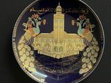 une image représentant une assiette décorative ornée de paons, avec un bâtiment en arrière-plan