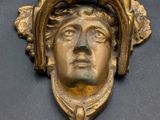 brass head of a man with a hat and a bell on a wall