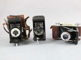 two old fashioned cameras sitting side by side on a white surface
