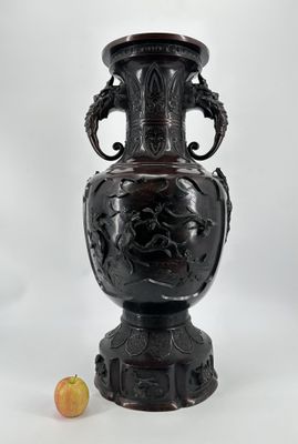 un grand vase noir posé à côté d'une pomme sur un fond blanc