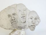 a sculpture of three faces on a rock with a white background
