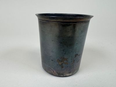une tasse en métal avec une anse posée sur une surface blanche