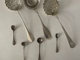 six silver spoons and a measuring spoon on a white surface