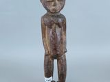une vieille statue en bois représentant un homme debout, les mains dans les poches