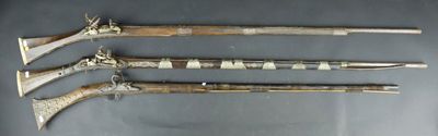 three old weapons are displayed on a table with a gray background