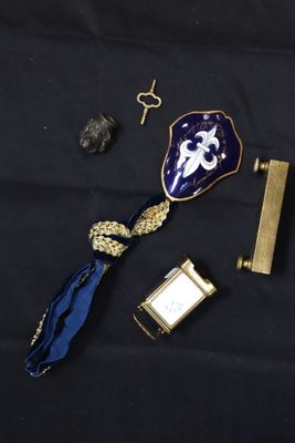 une cravate bleue et dorée sur laquelle figurent une horloge et d'autres motifs, posée sur un tissu noir