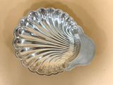 un plat argenté en forme de coquillage posé sur un fond beige