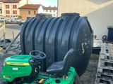 a green lawn mower parked next to a large black tank