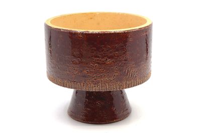 une petite tasse marron posée sur un socle, sur une surface blanche