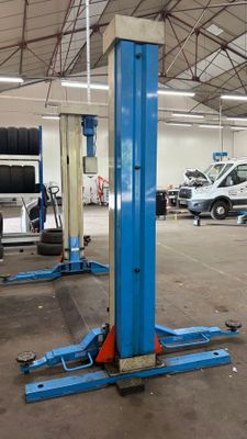 un pont élévateur bleu dans un garage, avec d'autres voitures en arrière-plan