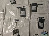 six white t - shirts with tags on them sitting on a bed